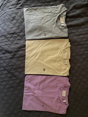 3-pack Gant t-shirts i olika färger - Säljer tre stilrena t-shirts från Gant i färgerna grå, beige och lila. Alla har klassisk passform, rund halsringning och Gant-logga broderad på bröstet. Perfekta basplagg i mjuk bomull som funkar till allt.