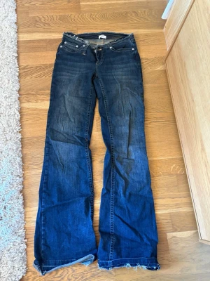 Blå bootcut jeans från Nelly - Säljer ett par blå bootcut jeans från Nelly med slitna detaljer och rå kant nedtill. Jeansen har klassisk femficksdesign och är gjorda i denim med snygg tvätt. Perfekta för dig som gillar en avslappnad och trendig look.