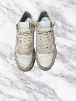  Philippe Model Sneakers  - Snygga sneakers från Philippe Model i vitt och beige. Skorna har en kombination av mocka och läder, med klassisk låg siluett och vita snören. Perfekta för en stilren och avslappnad look.