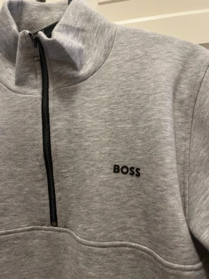 Grå halvzip hoodie från BOSS - Snygg ljusgrå hoodie från BOSS med halv dragkedja framtill. Storlek S .