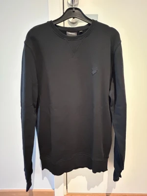 Svart sweatshirt Lyle&Scott - Stilren svart sweatshirt från Lyle & Scott  med rund halsringning och diskret broderad logga på bröstet. Tröjan har långa ärmar och ribbade muddar vid ärmslut och nederkant. Perfekt till ett avslappnat streetwear-look.
