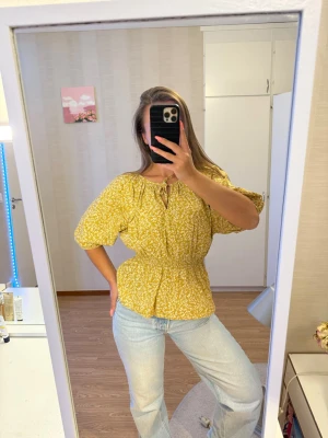 Lindex Gul blommig topp med puffärm - Säljer en söt gul blommig topp från H&M i storlek M. Toppen har puffärmar, resår i midjan och ett litet knytband vid halsen. Perfekt till våren och sommaren! Använd fåtal gånger och i mycket fint skick.