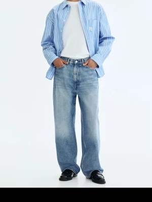 Blå raka jeans med lös passform - Säljer ett par ljusblå jeans med rak och lös passform. Jeansen har klassisk femficksdesign, normal midja och är tillverkade i denim. Säljer de då de tyvärr inte passade men är helt nya och oanvända med prislapp kvar. Sitter ungefär som storlek M för Män. Nypris 400 kr. 