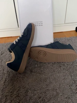 Mörkblå maison margiellas - Snygga mörkblå sneakers med beige gummisula och vita snören. Ovandelen är i mockaliknande material och insidan är ljusbeige. Klassisk låg modell som passar till det mesta och har en stilren design. Storlek 42. Helt nya 
