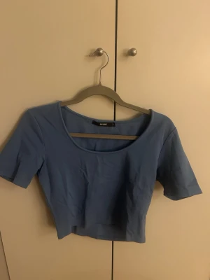 Ljusblå croppad topp med kort ärm - Säljer en ljusblå croppad topp med korta ärmar och rundad urringning. Toppen har en enkel och stilren design som passar perfekt till jeans eller kjol. Materialet är mjukt och tröjan är liten i storleken💋