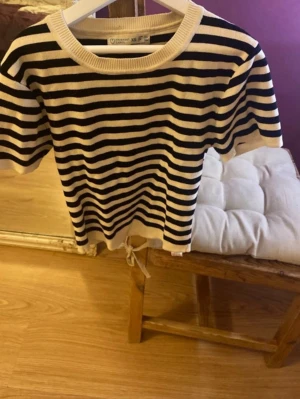 Randig kortärmad topp med knyt - Säljer en svartvit randig topp med korta ärmar och rund hals. Toppen har ett knytband nertill för en snygg detalj och är i mjukt material som känns skönt mot huden. Perfekt för dig som gillar en enkel men trendig look.