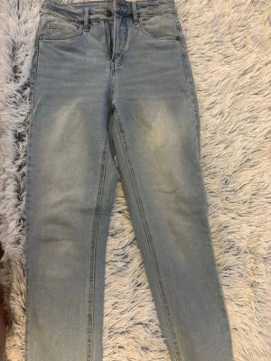 Ljusblå raka jeans med hög midja - Säljer ett par ljusblå jeans med raka ben och hög midja. Jeansen har klassisk femficksdesign, bälteshällor och dragkedjegylf. Materialet är mjukt denim i bomull och passformen är relaxed. Perfekta för en chill och trendig look.