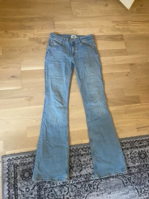Ljusblå bootcut jeans - Säljer ett par ljusblå bootcut jeans med klassisk femficksdesign och normalhög midja. Jeansen har utsvängda ben och är tillverkade i ett mjukt denimtyg som ger en avslappnad look. Perfekta för dig som gillar retrostil och vill ha ett par bekväma jeans.