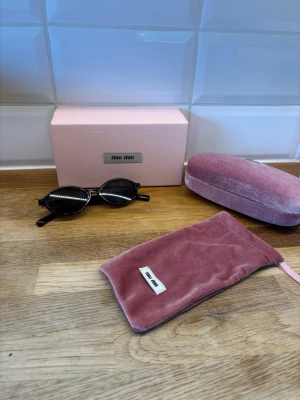 Miu miu solglasögon  - Snygga svarta solglasögon från Miu Miu med ovala bågar och mörka glas. Perfekta för dig som vill ha en trendig accessoar med lyxig känsla. (Bara solglasögon ingår)