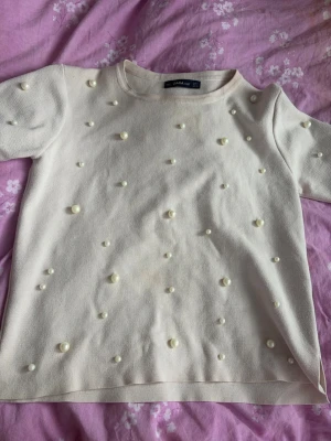 Vit topp med pärlor från Zara - Supersöt beige rosa topp från Zara med korta ärmar och dekorativa pärlor över hela tröjan. Har bara andtvänts ett fåtal gånger. 