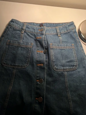 Jeanskjol med knappar från Divided - Snygg blå jeanskjol från Divided med stora framfickor och knappar längs hela framsidan. hör av dig om du ä intresserad💓!