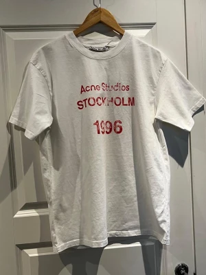 Acne studio vit  1996 T-shirt  - Tjena, säljer denna skitsnygga acne studios T-shirten från deras Stockholm 1996 modell med ljusrosa tryck, på bilden ser den mörkröd ut men de e någon kamera setting elr nåt. Enligt mig den snyggaste modellen. Tröjan är i storlek S och passar perfekt med allt och även året runt. Skriv gärna vid intresse! Köpt här på Plick o säljer vidare.