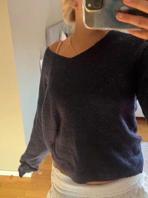 Mörkblå stickad tröja med v-ringning - Mysig mörkblå stickad tröja med avslappnad passform och v-ringad hals. Tröjan har långa ärmar och är gjord i ett mjukt, grovt stickat material. Perfekt för lager på lager och enkel att styla till olika outfits.