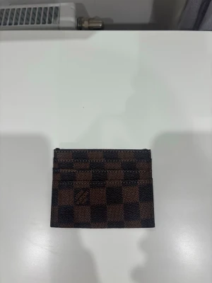 Brun och svart kortfodral - Snyggt kortfodral i brunt och svart med mönster. Fodralet har flera fack för kort och är tillverkat i ett tåligt material som liknar läder. Perfekt för dig som vill ha ett stilrent och smidigt sätt att bära dina kort.