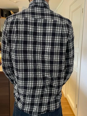 Svartvit rutig skjorta - Klassisk svartvit rutig skjorta med lång ärm och bröstficka. Skjortan har knäppning framtill och en avslappnad passform. Perfekt för dig som gillar en tidlös och enkel stil. Tillverkad i mjukt tyg som känns skönt mot huden.