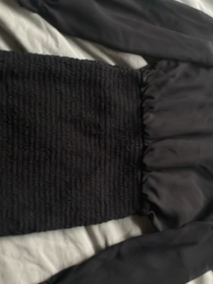 Svart långärmad klänning - Säljer en svart långärmad klänning med smockad midja och släta ärmar. Klänningen har en enkel och stilren design som passar perfekt till många olika tillfällen. Materialet känns mjukt och följsamt.