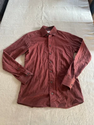 Eton slim fit skjorta - Säljer en snygg röd skjorta från Eton i slim fit-modell. Skjortan har långa ärmar, klassisk krage och knappar framtill. Tillverkad i mjuk bomull och passar perfekt för dig som gillar stilrena plagg med en modern touch.