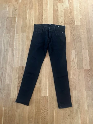 Svarta slim fit jeans från Replay - Säljer ett par svarta skinny jeans från Replay i storlek 30. Jeansen har klassisk femficksdesign, smal passform och är tillverkade i stretchigt denimtyg för extra komfort. Perfekta för en trendig och avslappnad look.