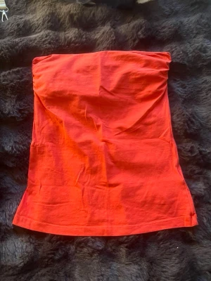 Axelbandslös tubtopp - Snygg röd tubtopp i mjukt bomullsmaterial. Toppen är axelbandslös och har en enkel, clean design utan mönster eller detaljer. Perfekt att styla till jeans eller kjol för en trendig look.