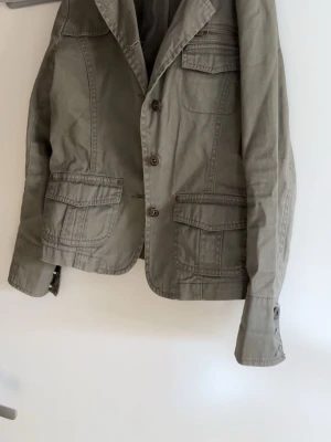 Kavaj / jeans jacka  - Stilren olivgrön kavaj med tre framfickor och knappstängning. Klassisk krage och sprund bak för extra rörelsefrihet. Perfekt för en avslappnad men ändå uppklädd look. I storlek 150 men passar även som ca xs