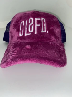 Lila fluffig keps från Classified - Säljer en unik lila keps från Classified med mjuk, fluffig yta och vit broderad text framtill. Baksidan är i mesh för extra ventilation och kepsen har justerbar passform. Perfekt för dig som vill sticka ut med en färgstark accessoar.