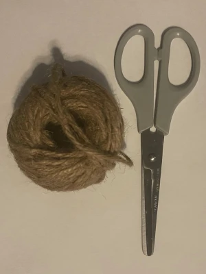 Grå sax och boll med jutesnöre - Säljer en enkel grå sax med plastgrepp och en boll med naturfärgat jutesnöre. Perfekt för pyssel, paketinslagning eller andra kreativa projekt där du behöver klippa och knyta. Saxen har rundade spetsar och snöret är grovt och slitstarkt.