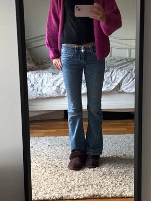 Blå bootcut jeans med låg midja - Säljer ett par blå bootcut jeans med låg midja och klassisk femficksmodell. Jeansen har en snygg tvätt och lätt utsvängda ben, perfekta för en trendig look. 