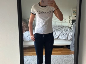 Vit t-shirt med svart text och detaljer - Säljer en vit t-shirt med svart text och illustrationer som stavar 'MONDAY' på bröstet. T-shirten har svarta kanter vid ärmslut och halsringning. Modellen är kortärmad och har en normal passform. Perfekt för dig som gillar enkla men snygga statement-plagg!💕tröjan har ett pyttelitet hål men som inte syns i helheten.