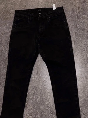 Svarta raka jeans - Säljer ett par svarta jeans med rak passform och klassisk femficksdesign. Jeansen har bälteshällor och knappgylf. Materialet är troligtvis bomull med lite stretch för extra komfort. Perfekta till en avslappnad och stilren look.