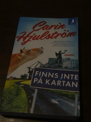 Finns inte på kartan av Carin Hjulström - Romanen 'Finns inte på kartan' av Carin Hjulström handlar om Frida Fors och hennes äventyr på landsbygden. Pocketbok med färgstarkt omslag som visar en ko, landsväg och vägskylt. Utgiven av Månpocket. Perfekt för dig som gillar svensk samtidslitteratur.