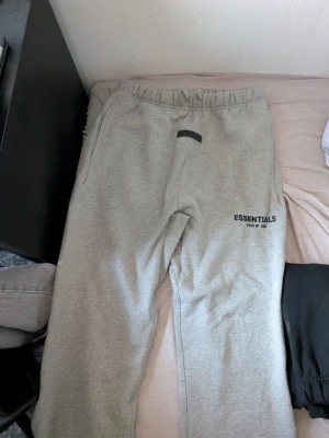 Grå Essentials FOG mjukisbyxor M - Säljer ett par grå mjukisbyxor från Essentials med tryck på vänster ben. Oanvända.
