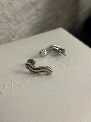 Silvriga vågformade örhängen - Säljer ett par stilrena örhängen i silverfärgad metall med vågig, modern design. Från Edblad 