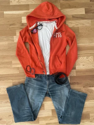 Hollister Hoodie Orange HERR XS/S - Orange Hollister hoodie i storlek S, men passar mer som XS. Har huva, dragkedja och snyggt Hollister-tryck framtill. Mjuk och skön hoodie i fint begagnat skick. Mått finns på de sista bilderna. Modell tillverkas inte längre. Säljs eftersom den inte passar längre.