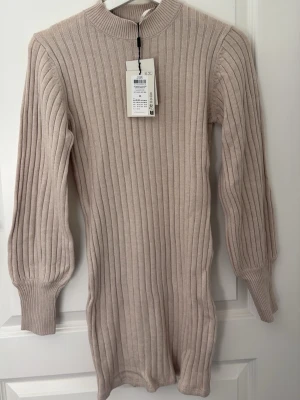 Beige ribbstickad klänning med puffärm - Klänningen är till knäna ungefär och är 76 cm lång från och med axeln. Den är väldigt stretchig och oanvänd.