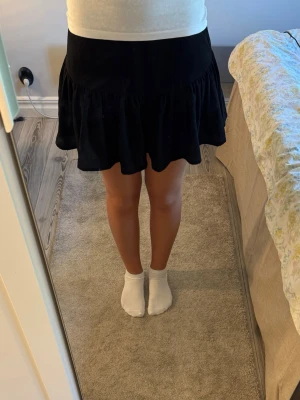 Svart volangkjol från Gina Tricot - Säljer en svart kortkjol från Gina Tricot i storlek XS. Kjolen har volangdetalj nedtill och resår i midjan för skön passform.  
