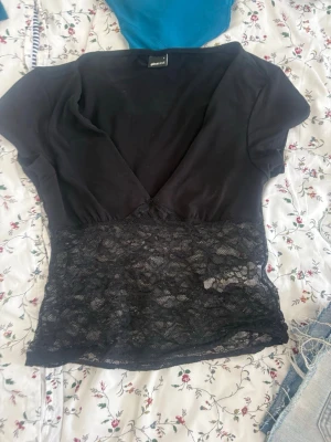 Svart topp med spets och v-ringning - Snygg svart topp med djup v-ringning och korta ärmar. Nedre delen är i transparent spets som ger en extra touch. Perfekt att styla med jeans eller kjol för en trendig look.