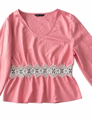 Rosa blus med spetsdetalj - Söt rosa blus från SHEIN med v-ringning och långärmad design. Blusen har en vit spetsdetalj i midjan med blommönster som ger en romantisk touch. Tillverkad i ett lätt tyg som ger ett fint fall.