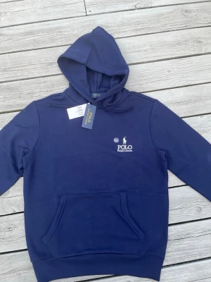 Blå hoodie från Polo Ralph Lauren - Polo Ralph Lauren hoodie – helt ny & oanvänd 🐎  Snygg marinblå hoodie från Polo Ralph Lauren med den klassiska vita, broderade Polo-loggan på bröstet.  • Helt ny och oanvänd • Marinblå med vit broderad logga • Huva och praktisk känguruficka • Ribbade muddar vid ärmslut och nederkant • Stilren modell som passar till både jeans, chinos och mjukisbyxor  Säljs eftersom jag fick den i present, men tyvärr passade den inte.  Nypris: 2395 kr Storlek: S  Skickas snabbt och packas ordentligt 