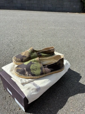 Riktigt feta Kamo-espadrillos från Valentino - Säljer ett par stilrena espadrillos från Valentino med kamouflagemönster i grönt, brunt och svart. Skorna har klassisk flätad sula och är tillverkade i canvas. Perfekta för dig som vill ha en unik och trendig look. Obs box ingår inte