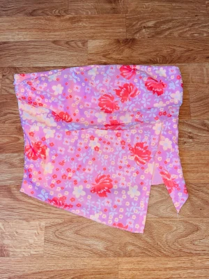 Blommig asymmetrisk tubtopp - En färgglad tubtopp med blommigt mönster i rosa, rött och gult. Toppen har en asymmetrisk nederkant.