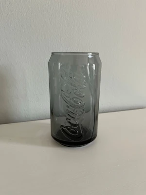 Coca-Cola Glas i svart / grå / sotig ton - Limited Edition 2008 - McDonald’s - Samlarglas - Coca-Cola samlarglas från McDonald’s, i en svart/grå, sotig ton. Glaset är format som en Coca-Cola-burk. Ett samlarobjekt för Coca-Cola-entusiasten, men fungerar självklart även utmärkt som vanligt dricksglas! Limited Edition 2008. Stämplat med ”IA” i botten. Höjd: ca 12 cm. Diameter: ca 6 cm. Säljs i bra skick! Jag kan själv inte se några uppenbara nagg eller sprickor, men observera att detta glas är använt! Kika gärna in på mina andra annonser, jag säljer just nu flera olika glas och muggar!