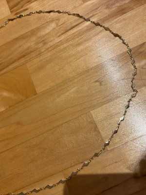 Guldfärgad magkedja med zickzack-länkar - Snygg magkedja i guldfärg med unika zickzack-formade länkar. Magkedjan har en tunn och elegant design som sticker ut med sina geometriska former. Perfekt för dig som gillar stilrena och moderna accessoarer.
