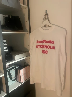 Vit Acne Studios t-shirt med tryck - Vit t-shirt från Acne Studios med rosa fluff tryck (gammal kollektion). Jättenajs lite oversised i storlek S som passar de flesta! Säljer på grund av att jag måste tjäna pengar, hade behållt annars då den e i bra skick och inte använd alls!! 