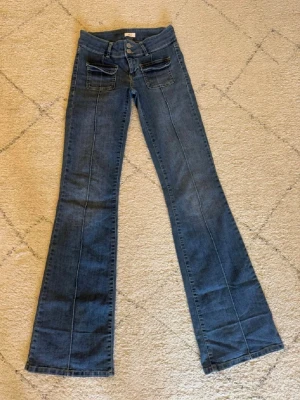 Low waist jeans  - Snygga blå bootcut jeans med markerade sömmar och två stora fickor framtill. Jeansen har utsvängda ben och klassisk femficksdesign baktill. Tillverkade i denim med en cool vintagekänsla och hög midja.