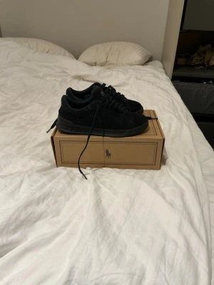Mörkblå Polo Ralph Lauren sneakers - Snygga mörkblå sneakers från Polo Ralph Lauren i mocka med klassisk låg profil. Skorna har blå snören och Polo-logga på plösen. Perfekta för dig som gillar stilrena och tidlösa sneakers med en sportig touch.