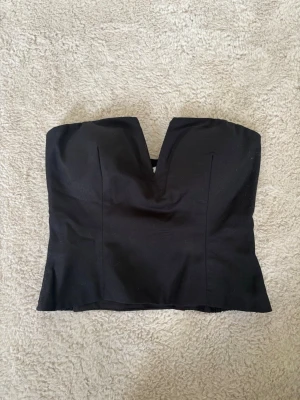 Svart topp - Svart topp från NA-KD, stretchigt material, dragkedja på sidan, vadderade kupor med silicon kant så den inte glider ner, lite kortare i modellen