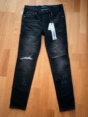 Purple beans jeans  - Säljer ett par svarta skinny jeans med slitningar över knäna och små vita färgstänk framtill. Jeansen har fem fickor, orangea nitar och en tvättad look. Perfekta för dig som gillar en edgy och trendig stil.