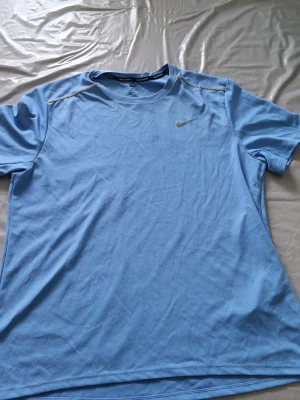 Ljusblå Nike tränings Miler - Säljer en ljusblå tränings-tshirt från Nike med klassisk silverfärgad swoosh på bröstet. T-shirten har rund hals, korta ärmar och är gjord i ett lätt, ventilerande funktionsmaterial som passar perfekt till träning.