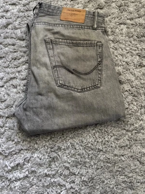 Grå jeans från Jack & Jones - Snygga grå jeans från Jack & Jones i klassisk femficksmodell. Jeansen har raka ben och en cool tvättad look med kontrastsömmar och patch bak i midjan. Perfekta till en avslappnad stil. Dock lite slita som de syns i sista bilden w29/l32