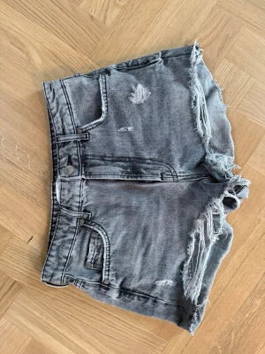 Grå slitna jeansshorts med fransar - Säljer ett par grå jeansshorts med slitna detaljer och fransig kant. Shortsen har fem fickor, knapp och dragkedja. Storlek 36 från Zara.